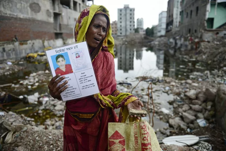A mourner holds up a portrait of a missing relative and a human bone fragment found at the scene of the 2013 Rana Plaza building collapse.jpg